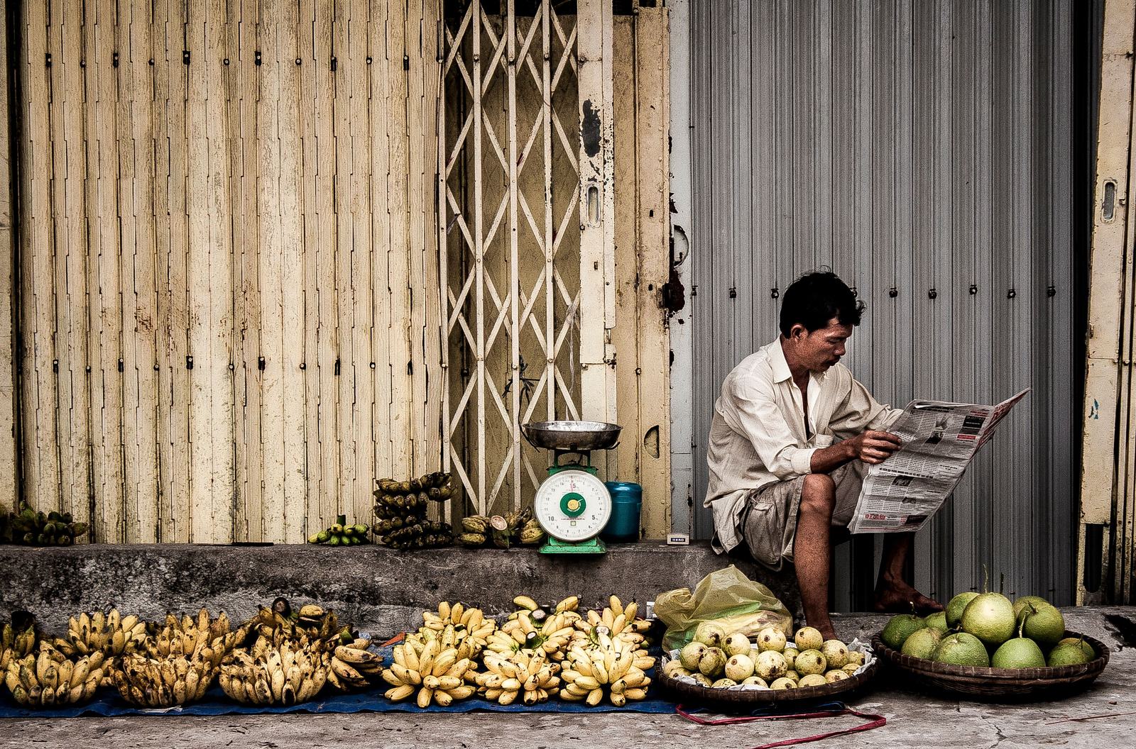 A street seller reading the paper beside his fruit